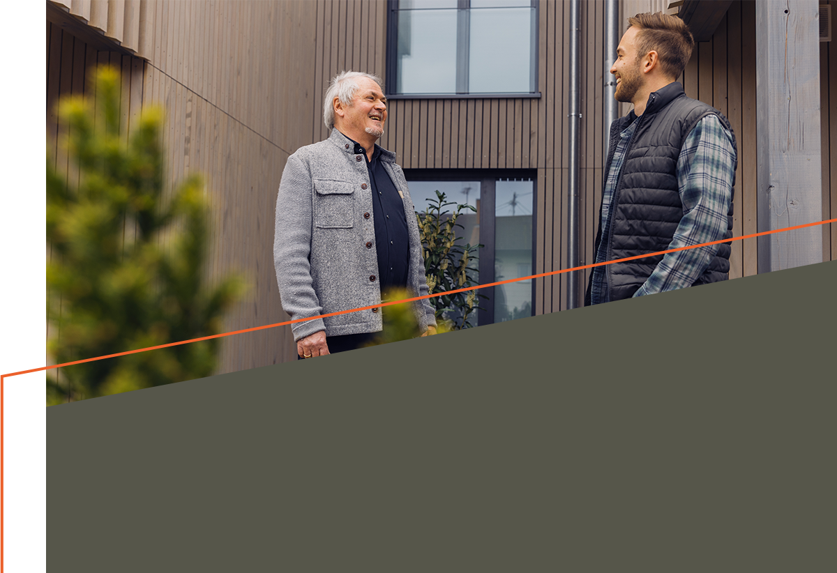 Eckhard Wolf und Jonas Luddeneit vor Holzfassade eines Wohnhauses