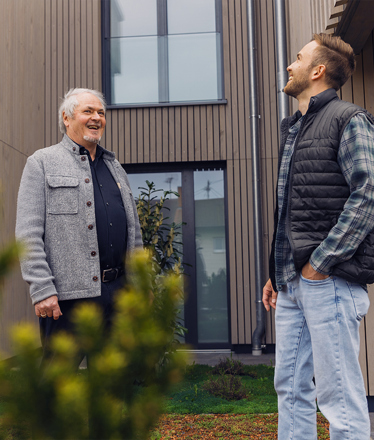 Eckhard Wolf und Jonas Luddeneit vor Holzfassade eines Wohnhauses.