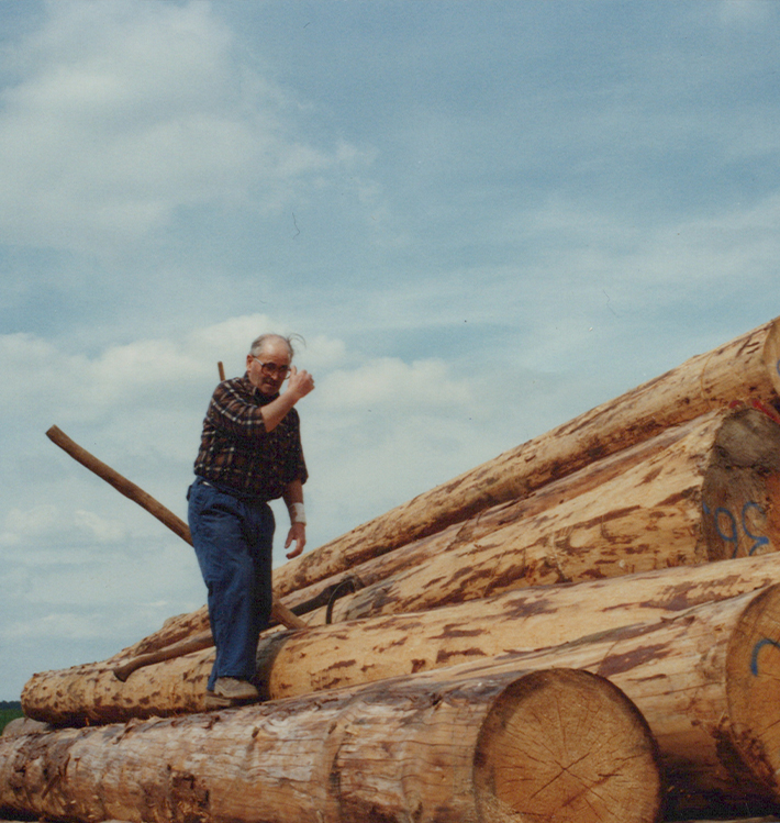 Gründer Werner Wolf auf einem Stapel Rundhölzer.